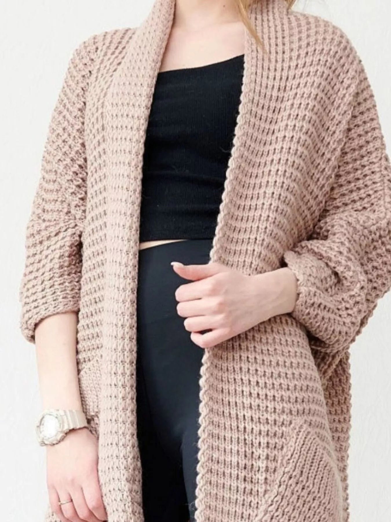 Woman wearing a blush-pink Chunky Knit Open Front Cardigan with a textured waffle weave and deep front pockets, styled over a black top.