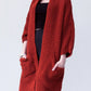 Woman wearing a cozy, rust-red Chunky Knit Open Front Cardigan with a textured waffle weave and deep front pockets, styled over a black outfit.
