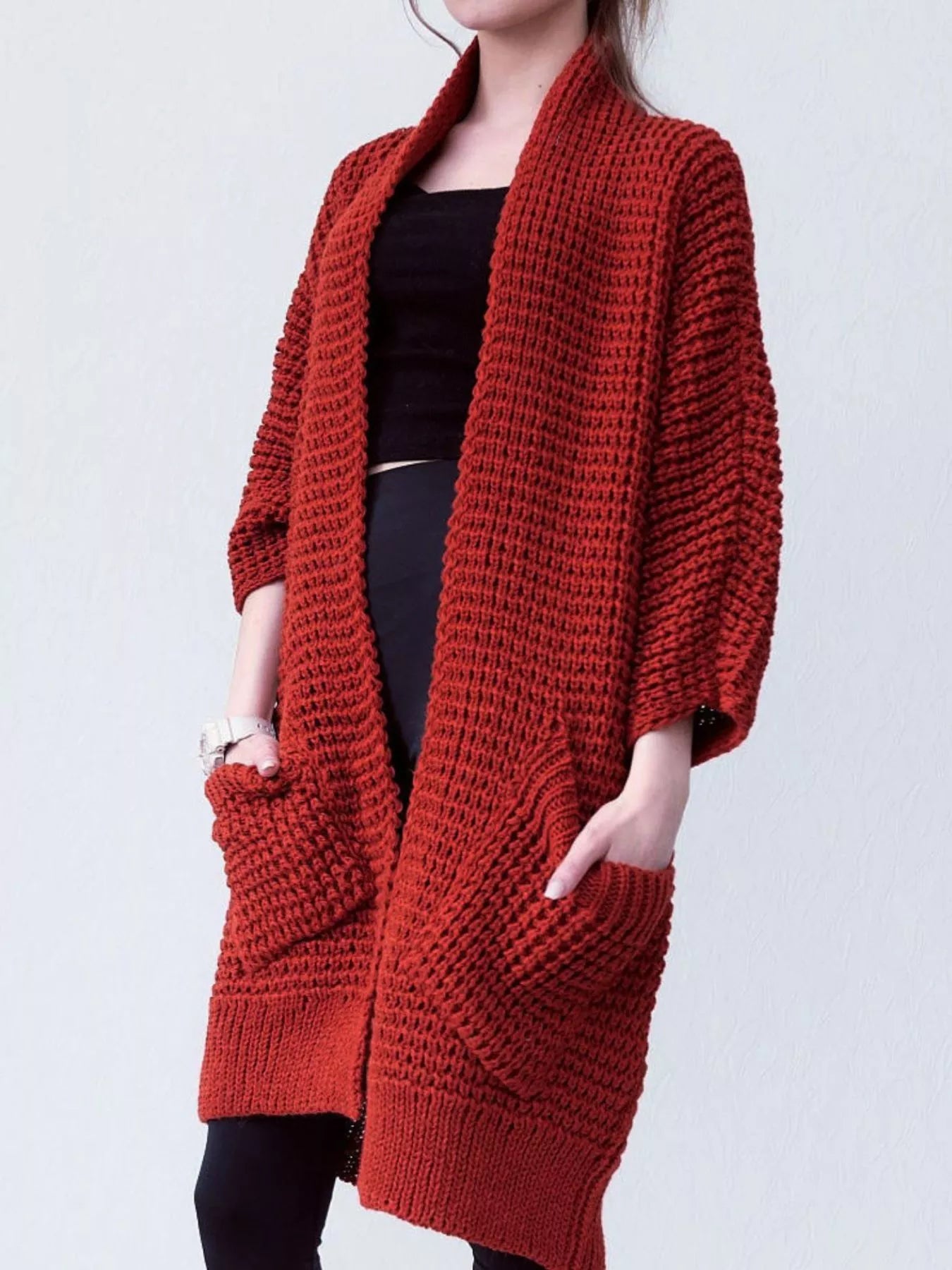 Woman wearing a cozy, rust-red Chunky Knit Open Front Cardigan with a textured waffle weave and deep front pockets, styled over a black outfit.