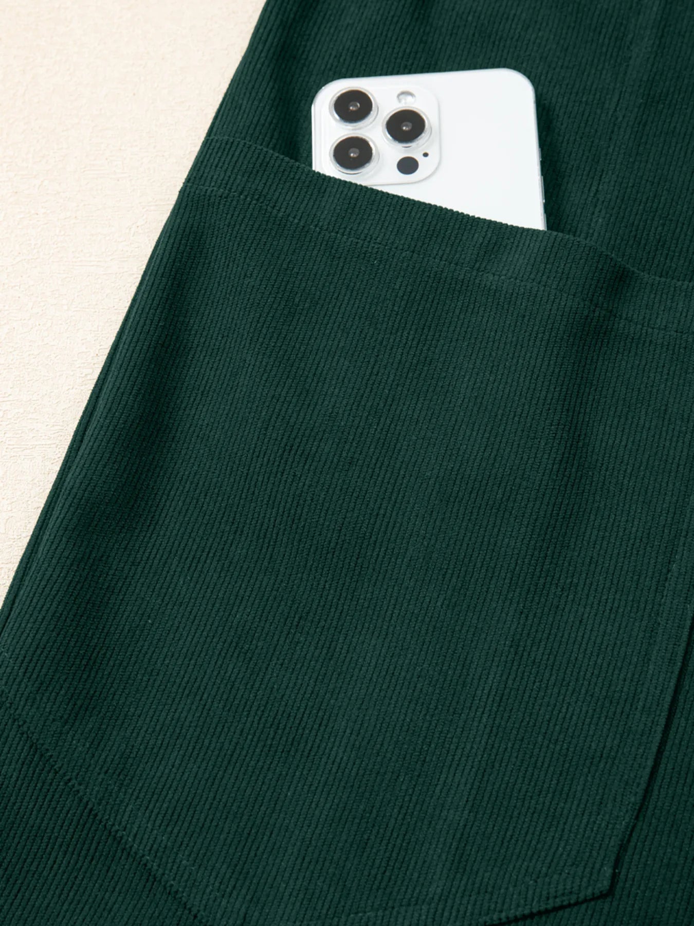 Dark green corduroy pocket with white smartphone in women’s jumpsuit