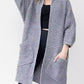 Woman wearing a cozy, longline gray chunky knit open-front cardigan with a textured waffle weave and large front pockets.