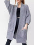 Woman wearing a cozy, longline gray chunky knit open-front cardigan with a textured waffle weave and large front pockets.
