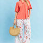 Woman in Umgee coral linen scallop trim V-neck blouse with white sea-print pants