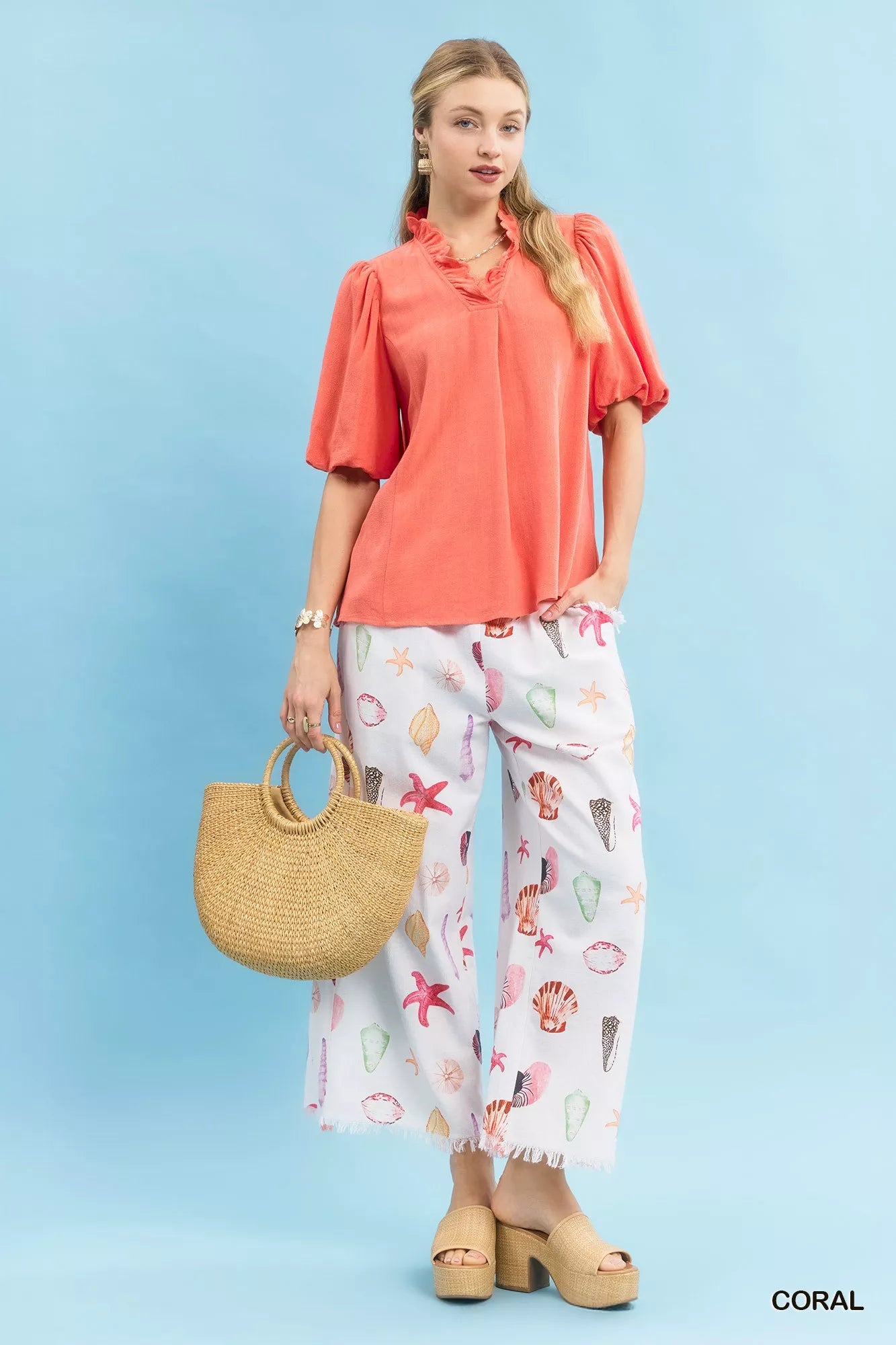 Woman in Umgee coral linen scallop trim V-neck blouse with white sea-print pants