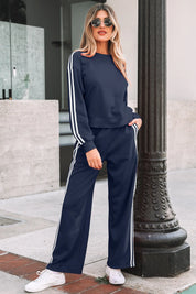 Woman wearing a navy tracksuit with white stripes standing outdoors.